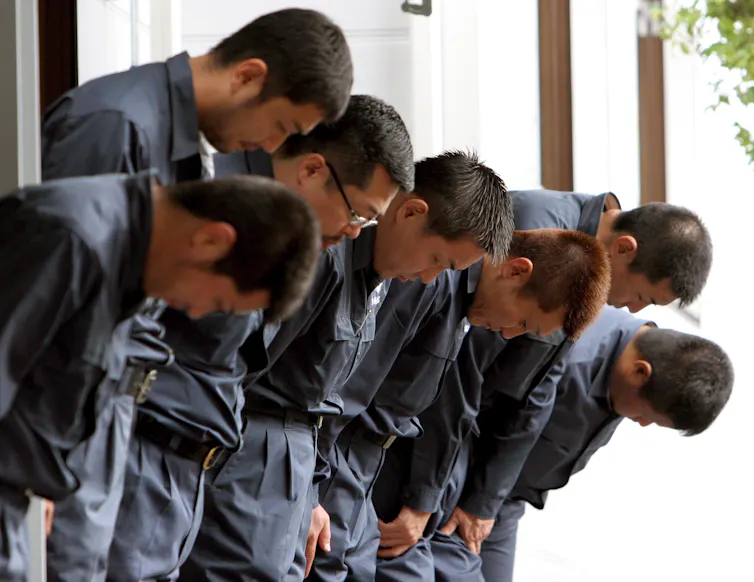 A row of young Japanese men make a ceremonial bow.