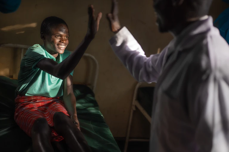 A young patient in a hospital bed grins broadly while giving a man in a white coat, who is a nurse, a high five