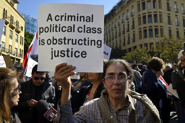 Una mujer en una multitud sostiene un cartel que dice "Una clase política criminal está obstruyendo la justicia".