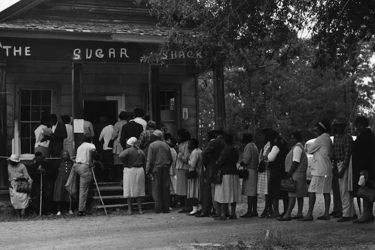 A group of about two dozen people lined up outside a rural store.