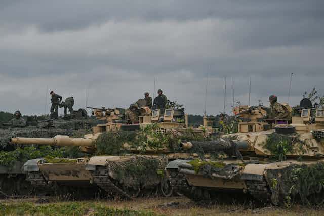 Soldiers wearing camouflage sit atop of beige tanks on a clo