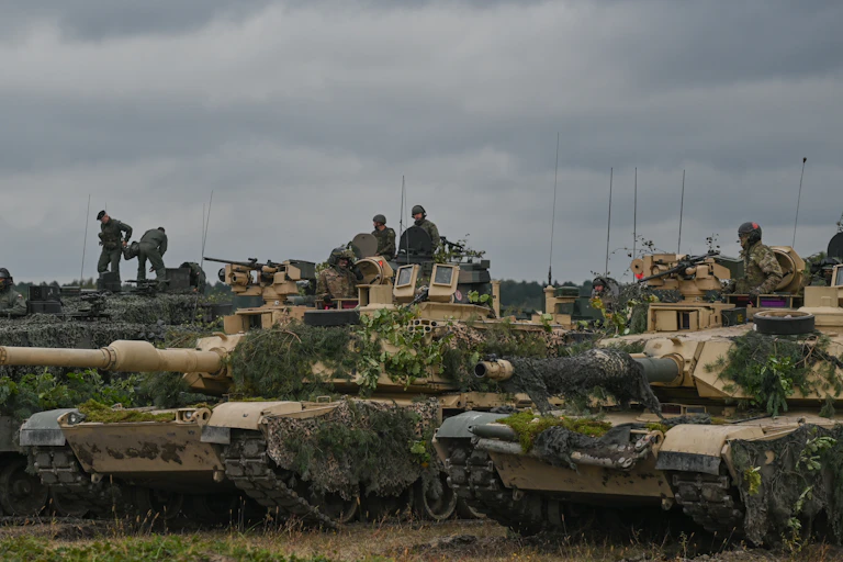 Soldiers wearing camouflage sit atop of beige tanks on a clo
