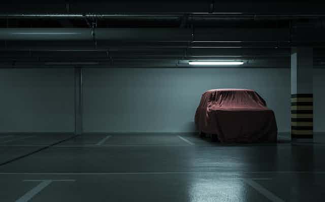 Car with a red cover sits in an otherwise empty parking garage.