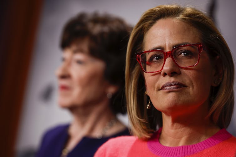 Two women from the shoulders up, one with short black hair and the other with medium length brown hair and glasses.