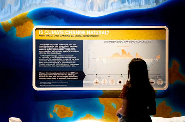 A child standing in front of a large display which has a question: Is climate change natural?