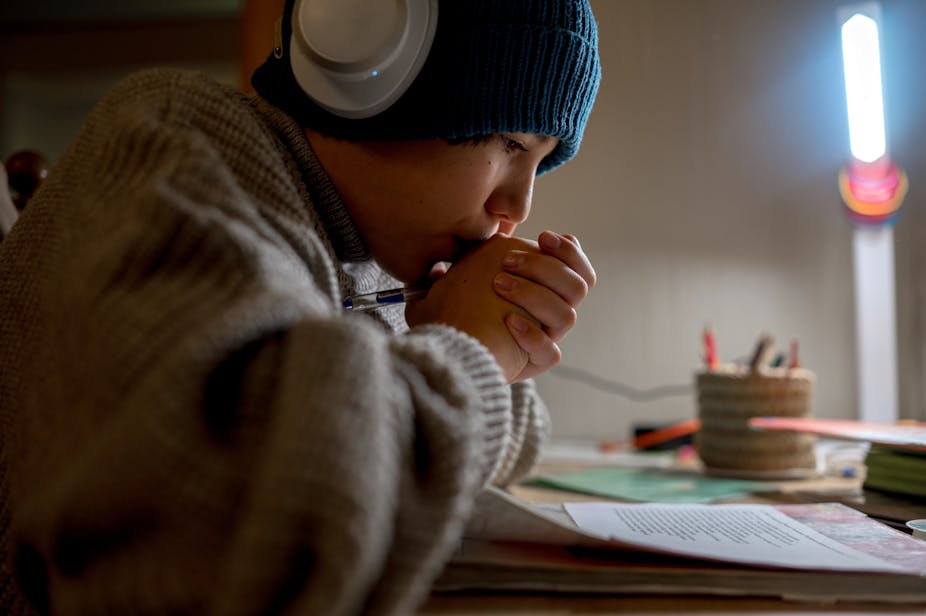 Un adolescent fait ses devoirs dans une pièce peu chauffée