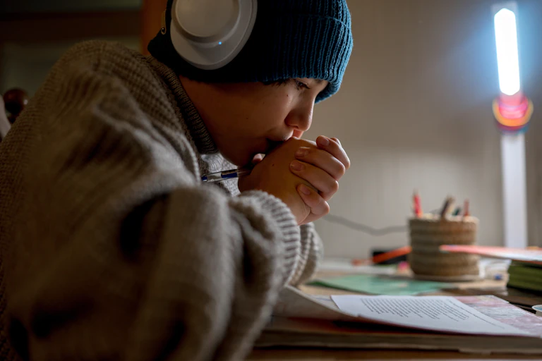 Un adolescent fait ses devoirs dans une pièce peu chauffée