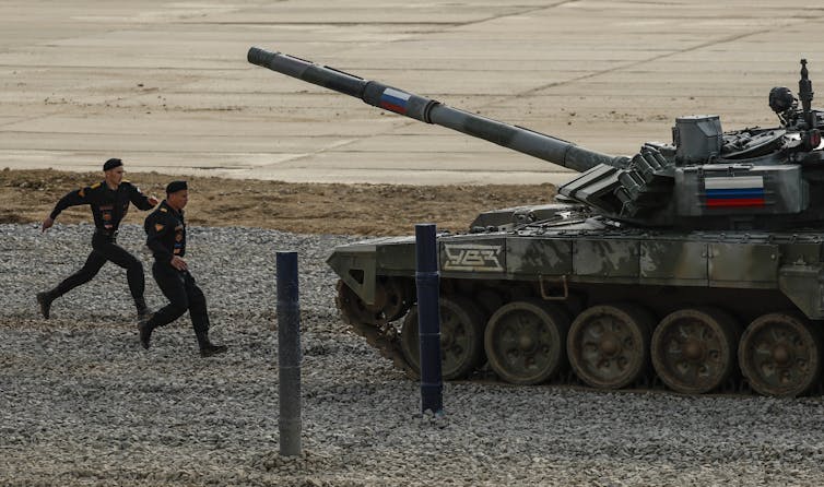 Two soldiers run towards a RussianT-72B3 main battle tank.