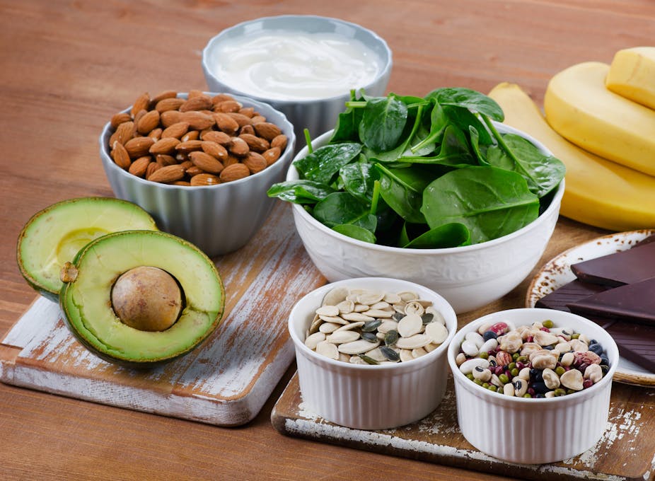An assortment of magnesium-rich foods on a table, including almonds, spinach, avocado, yoghurt and seeds.