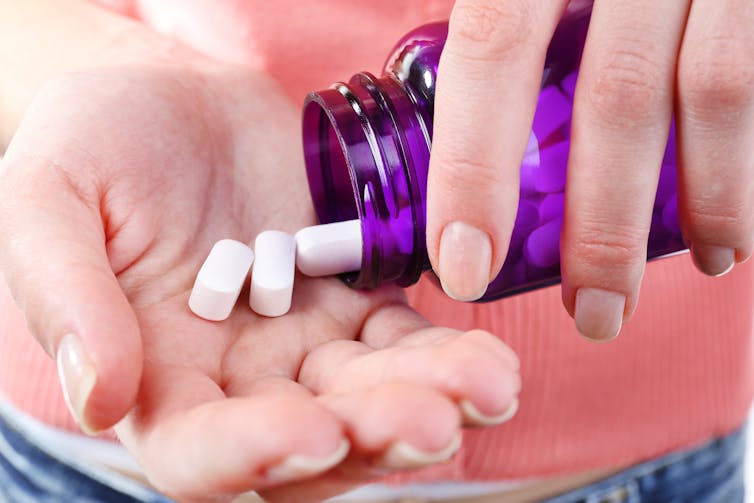 A person pours two white pills into the palm of their hand from a purple bottle.