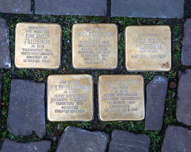 An overhead shot of five bronze memorial cobblestones with inscriptions.