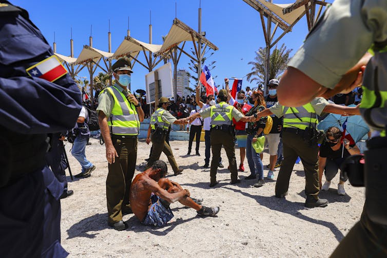 A man sits with his head bowed on a beach as police offers surround him.