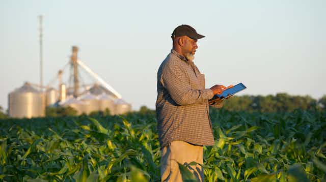 A man in a baseball cap clicks on a tablet device while standing in a field