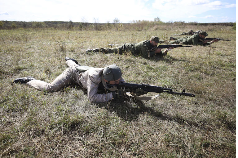 Des hommes en tenue de combat portant des armes avancent à plat ventre sur le sol lors d'un exercice d'entraînement.