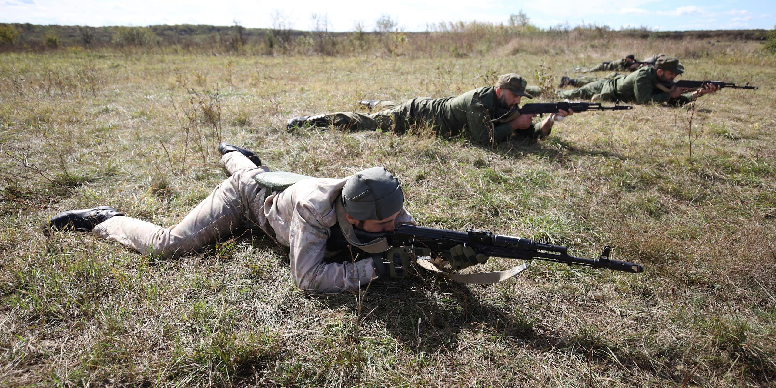 Des hommes en tenue de combat portant des armes avancent à plat ventre sur le sol lors d'un exercice d'entraînement.