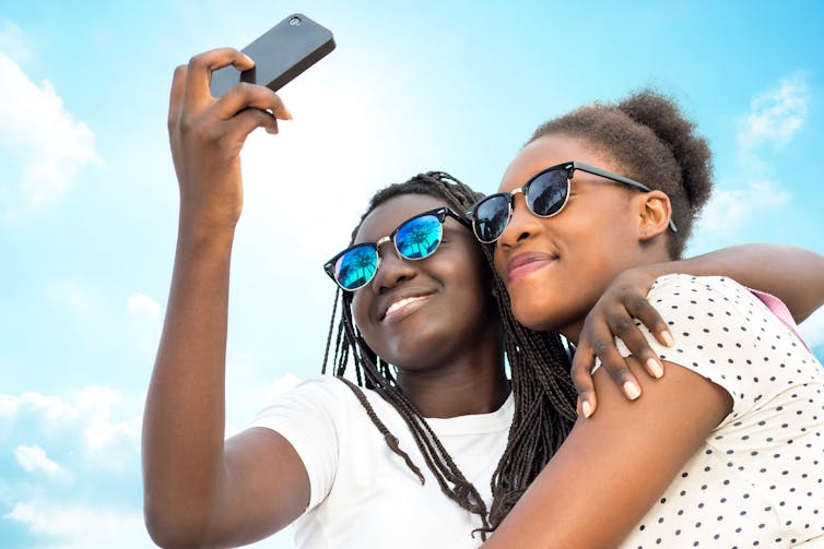 two teenage girls wearing sunglasses take a selfie