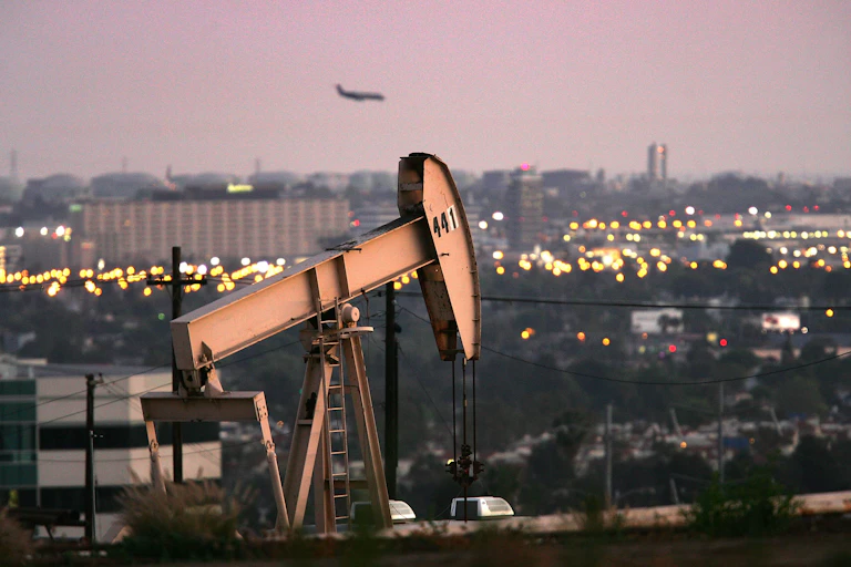 An oil pump with the city skyline behind it and offices nearby.