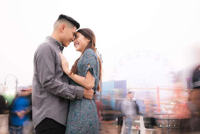 An East Asian man and woman hold each other while smiling.