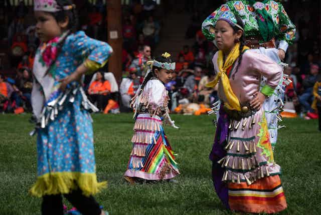 Young girls in jingle dresses perform a dance.
