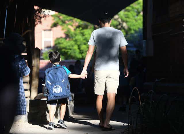 A parent holds the hand of a small child at school. 