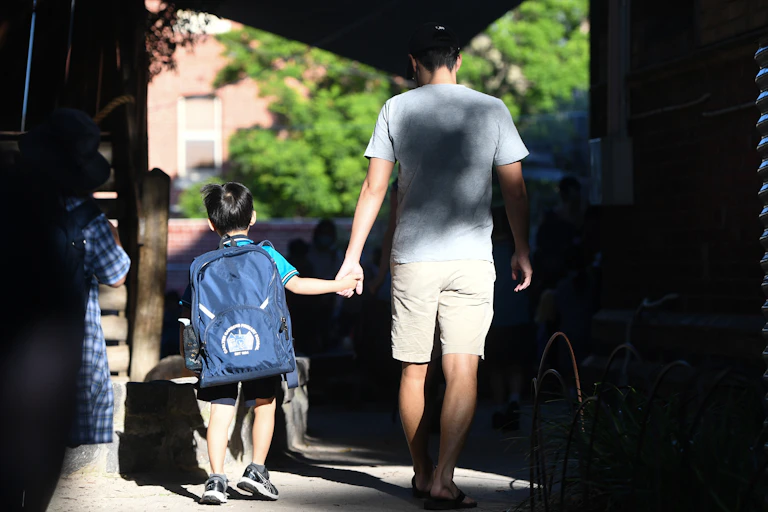 A parent holds the hand of a small child at school.