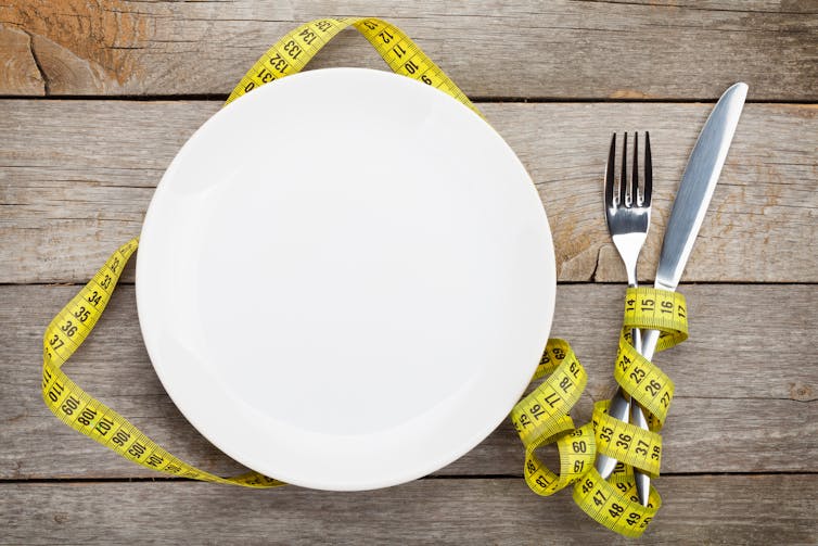 An empty plate and a knife and fork wrapped in measuring tape