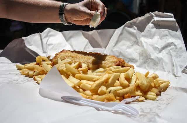 A person squeezes lemon on fish and chips.