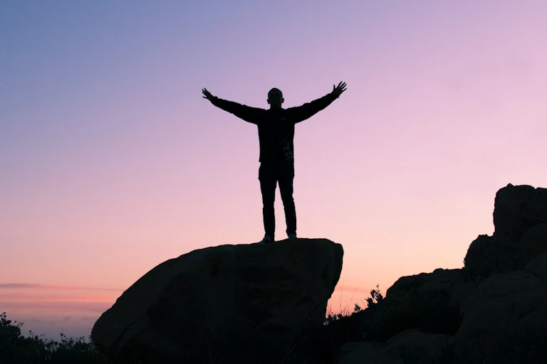 Homme levant les bras au sommet d'une montagne