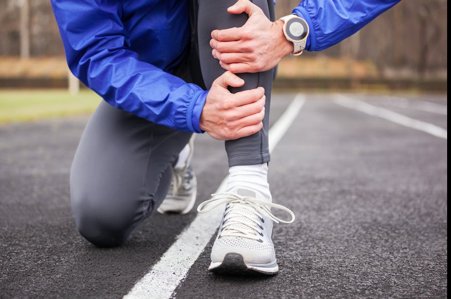 A person in running gear kneels on the ground, holding their shin in pain due to a shin splint.