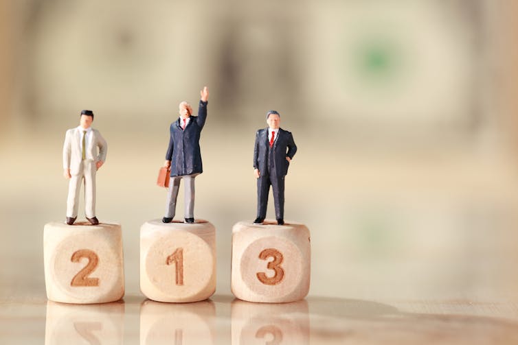 Miniature people: businessman standing on wooden podium with dollar bank note blur background