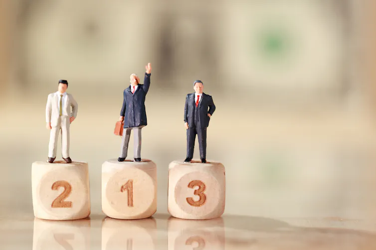 Miniature people: businessman standing on wooden podium with dollar bank note blur background