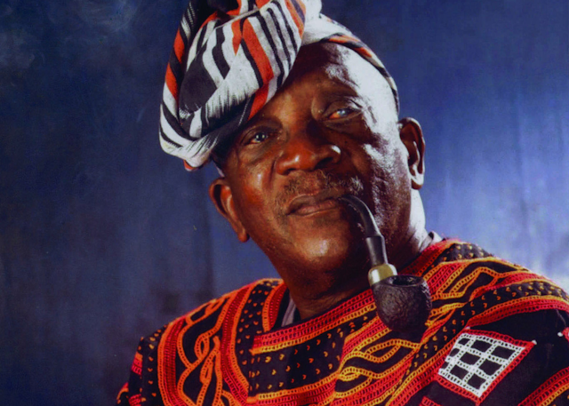 Man in traditional African clothes smoking a pipe.