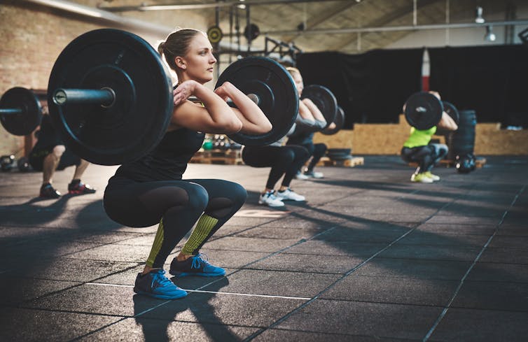 A young woman performs a barbell squat in a gym.