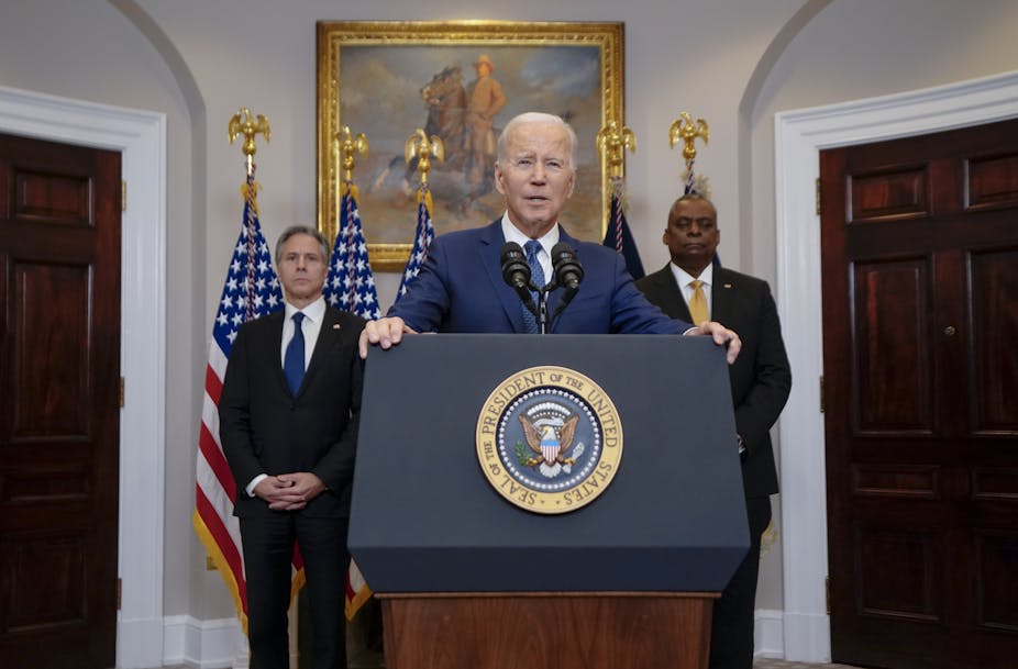 US president Joe Biden flanked by two aides stands at a lectern in the White House.
