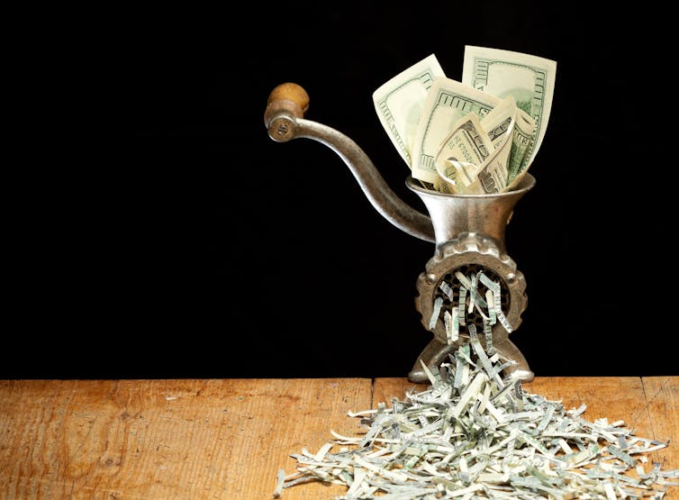 A mincer shows dollars being inserted in the top and shredded underneath.