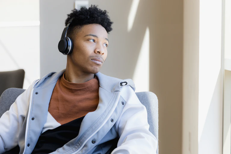 A young Black man wearing headphones looks out the window with a look of resignation.