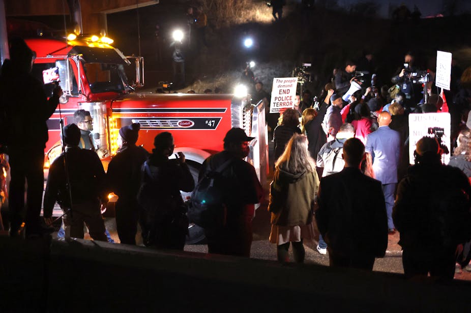 Protesters, some holding signs, block a red tractor trailer