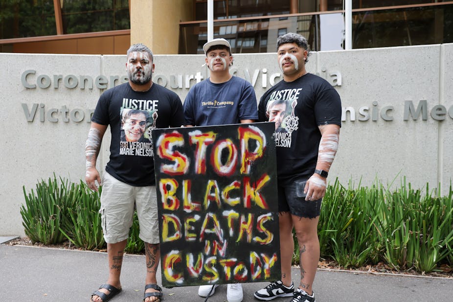 Indigenous community members standing outside the Victorian coroners court with a sign saying 'stop black deaths in custody'