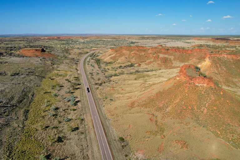 Aerial photo of the Great Northern Highway in Western Australia, among green and red hills.