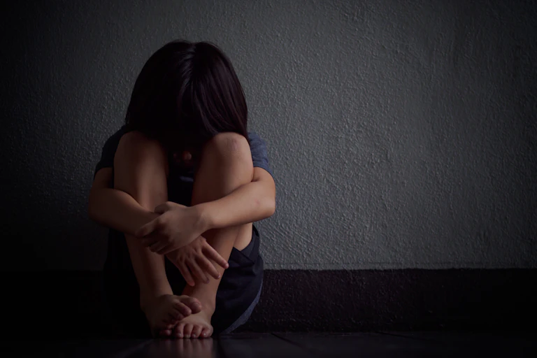 child hides face and sits against wall