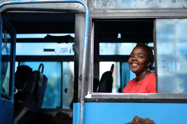 A young Kenyan woman smiles as she looks out of a bus window.