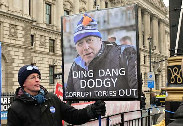 A protester holding a sign reading "ding dang dodgy. Corrupt tories out'