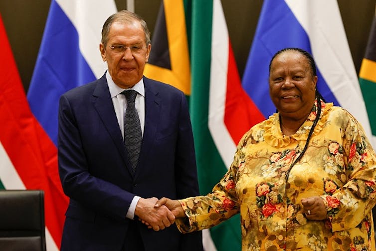 A man wearing a suit and tie shakes hands with a woman wearing a dress.