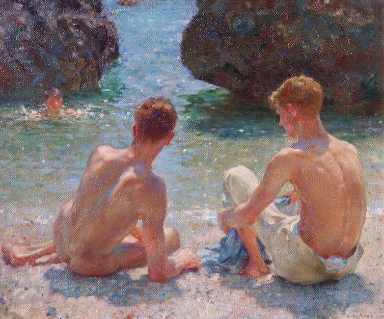 Two men sit on the beach, they are a couple, leaning into one another slightly.