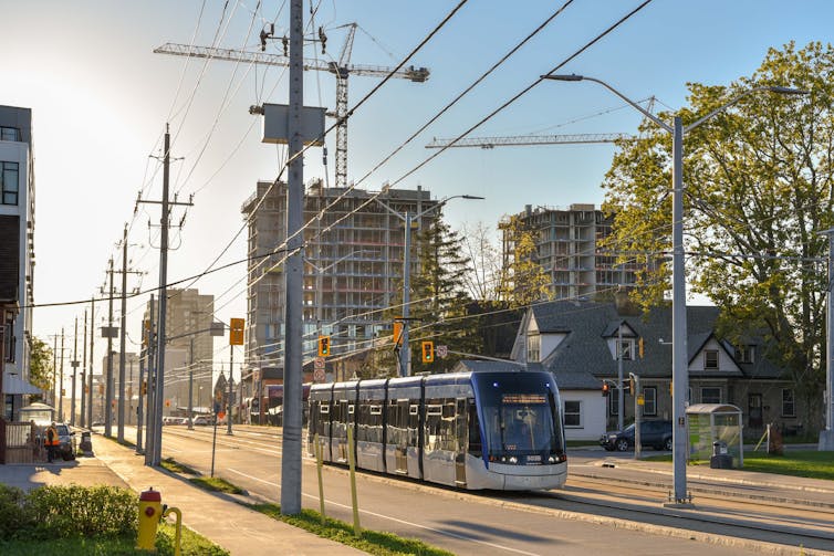 A street car drives down the centre of a two-way street. Condos and apartment buildings are seen in the background