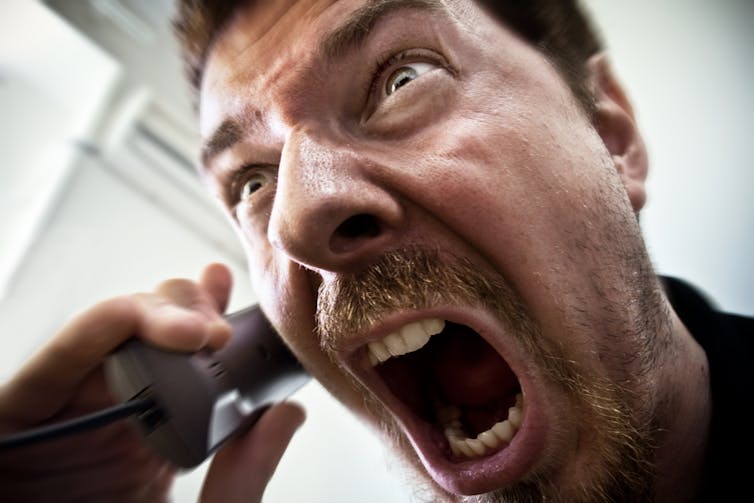 Stressed angry man with beard shouting into a phone.