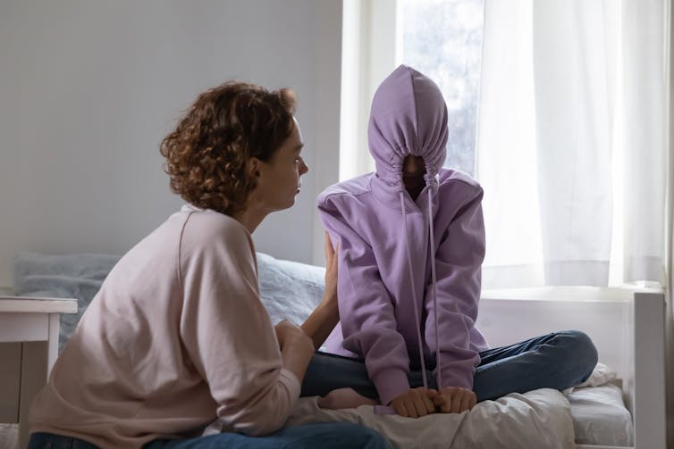 Mother talking to teenager, who has hoody drawn over their face.