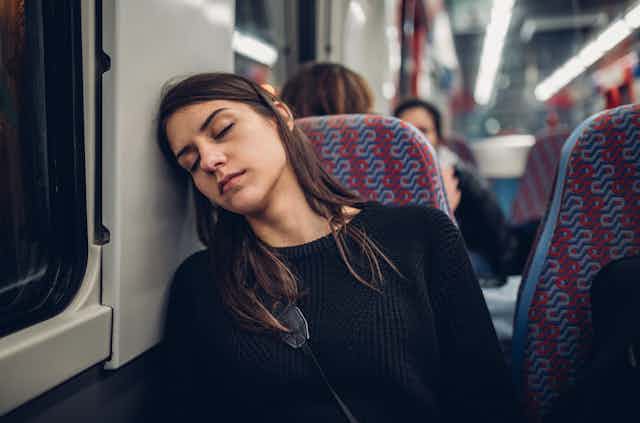 A young women is asleep on a train, resting her head against the window. 