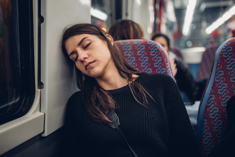 A young women is asleep on a train, resting her head against the window.