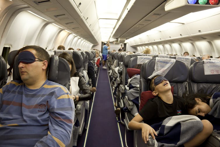 A view from the front of a cabin of various plane passengers sleeping with eye masks.